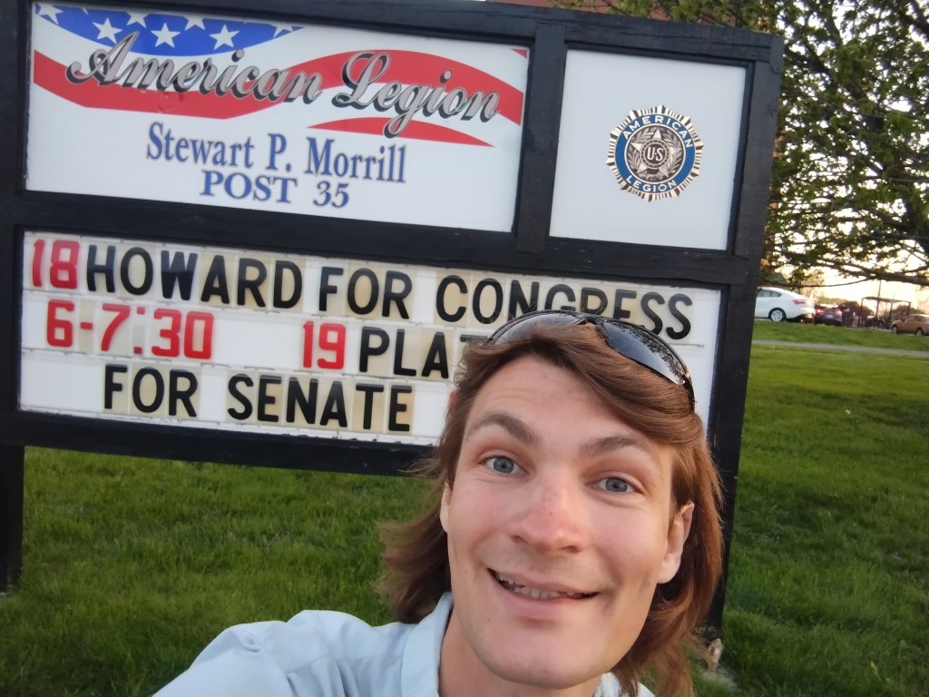 Tristram grinning in front of a sign reading "HOWARD FOR CONGRESS" posted in front of the American Legion Post 35 on Broadway. The American Legion does not sponsor or endorse my candidacy